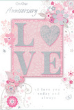 This romantic anniversary card appears like a delicate floral composition, the kind a Dollis Hill couple might exchange after years of shared walks through Gladstone Park. The cover is washed in a soft blush-pink tone, reminiscent of early evening light, against which the word LOVE stands boldly at the centre. Each letter is embossed and dusted with a fine, silvery-white glitter, giving the text a raised, tactile quality that catches the light in gentle glints rather than harsh sparkles. The texture suggests both luxury and tenderness, mimicking the glimmer you might see on satin ribbon laced through an anniversary bouquet. Flowing out from around this central word is an intricate pattern of illustrated flowers and leaves, their forms curling and unfurling in graceful lines. The blossoms are drawn in varying shades of pale pink, ivory, and cool grey, with some petals kissed by tiny touches of metallic silver that create a quiet, refined sheen. Thin, swirling stems and trailing foliage wind across the surface, balancing open spaces with detailed clusters, much like a carefully balanced hand-tied arrangement. A few stylised butterflies and small flourishes seem to hover among the blooms, adding a sense of lightness and quiet joy. The overall design feels airy, romantic, and slightly ethereal, as though a florist had sketched a bouquet straight onto the card. Inside, the scripted message - expressing ongoing devotion and love today and always - is printed in an elegant, flowing font. The card as a whole feels like a keepsake of enduring affection, perfect for marking a special anniversary within a cosy Dollis Hill home.